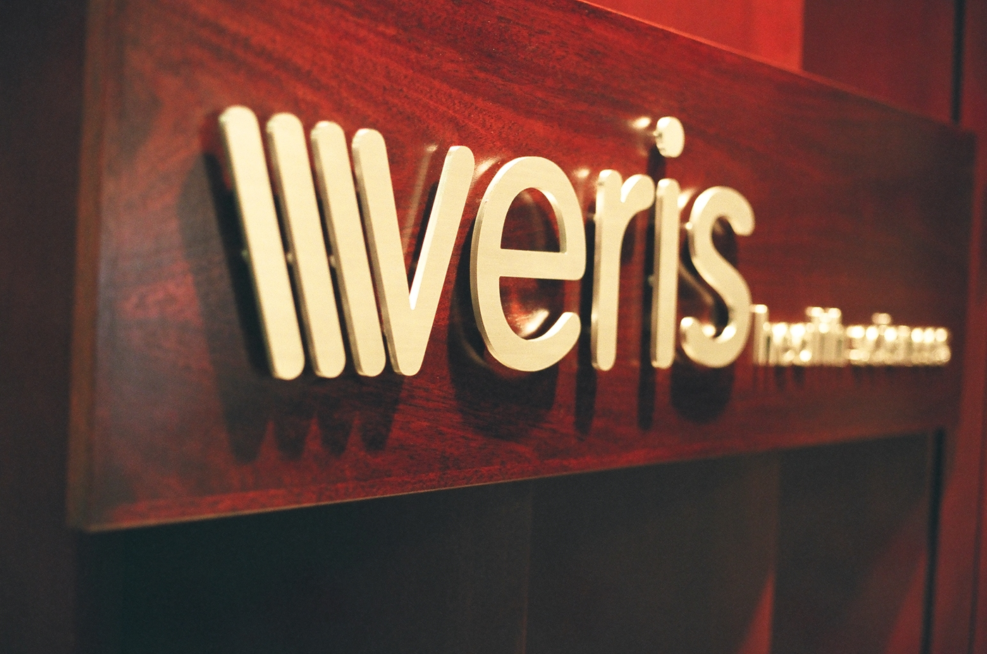 Polished brass flat cut letters and logo for Veris Health Sciences on a mahogany reception panel